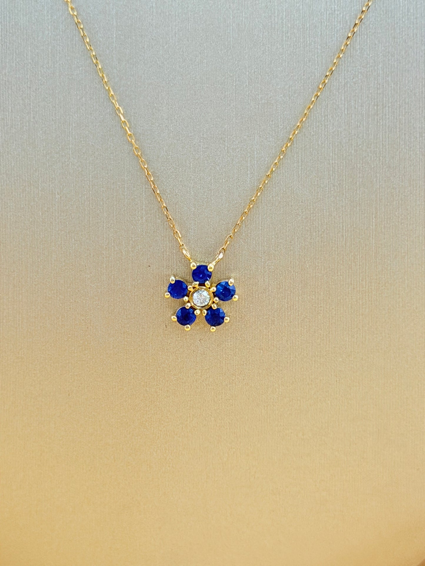 14kt gold necklace with a flower pendant, featuring a sapphire and natural diamond. 0.03 ct of natural diamonds and 0.36 ct of sapphire. Size 16”-18”